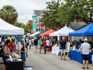 A colorful scene from the Charleston Black Expo with attendees interacting and local vendors showcased.