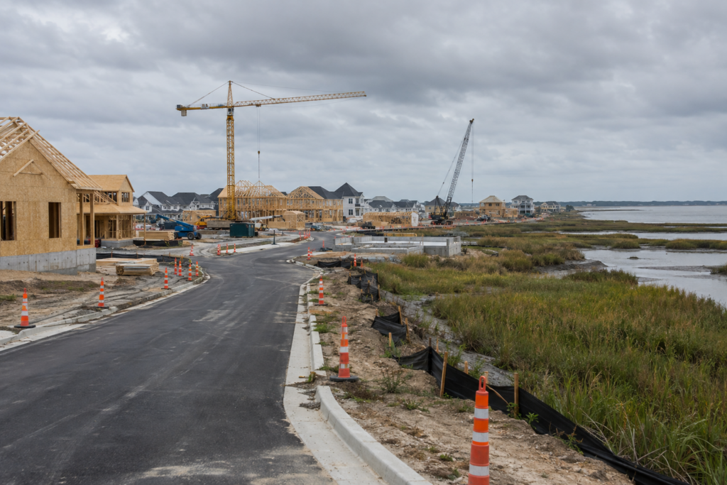 Homes under construction with cranes near coastal marsh along a growth corridor